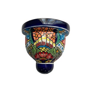 May include: A hand-painted ceramic wall pocket with a vibrant floral design. The piece features a deep blue rim and base, with a colorful pattern of orange, yellow, green, and red flowers. The wall pocket is a decorative item.