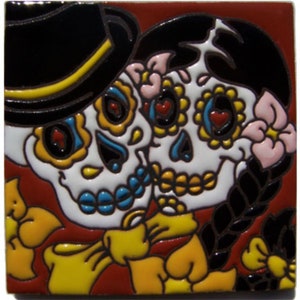 May include: A colorful ceramic tile featuring a couple of sugar skulls with floral accents. The male skull wears a black top hat and the female skull has a black braid. The tile has a red background.
