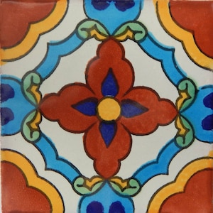 May include: Square ceramic tile with a symmetrical floral design. The central flower is red with a yellow center and blue accents. The design includes blue, yellow, and green elements on a white background, framed by red corners.