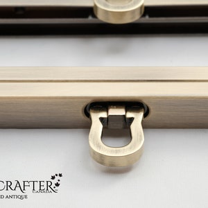 May include: A close-up of a brushed antique gold metal frame with a D-ring closure. The frame is made by Luxcrafter Canada.