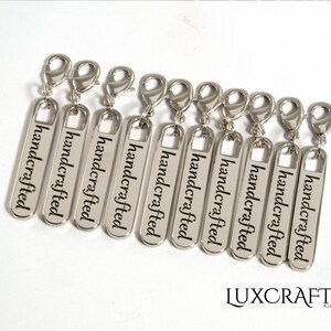 Puede incluir: Ocho tiradores de cremallera plateados con la palabra "handcrafted" grabada en cada uno.