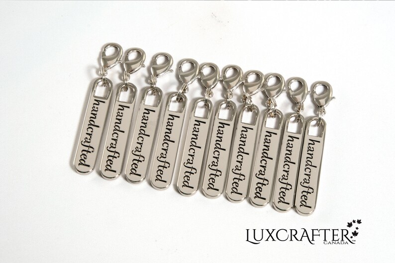 Puede incluir: Ocho tiradores de cremallera plateados con la palabra "handcrafted" grabada en cada uno.