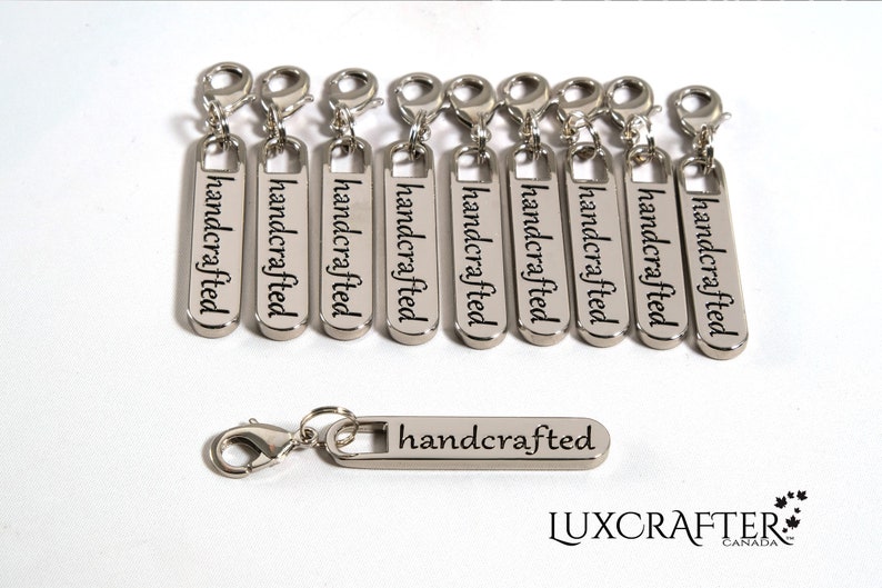 Puede incluir: Diez tiradores de cremallera plateados con la palabra "handcrafted" grabada en cada uno. Los tiradores de cremallera est&aacute;n dispuestos en una fila. Hay un tirador de cremallera adicional debajo de la fila, tambi&eacute;n con la palabra "handcrafted" grabada en &eacute;l. La palabra "LUXCRAFTER" est&aacute; impresa debajo de los tiradores de cremallera.