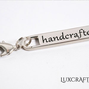 Puede incluir: Tirador de cremallera plateado con un cierre de langosta plateado y la palabra "handcrafted" grabada en el tirador.