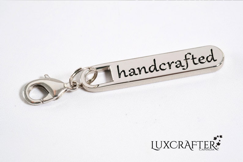 Puede incluir: Tirador de cremallera plateado con un cierre de langosta plateado y la palabra "handcrafted" grabada en el tirador.