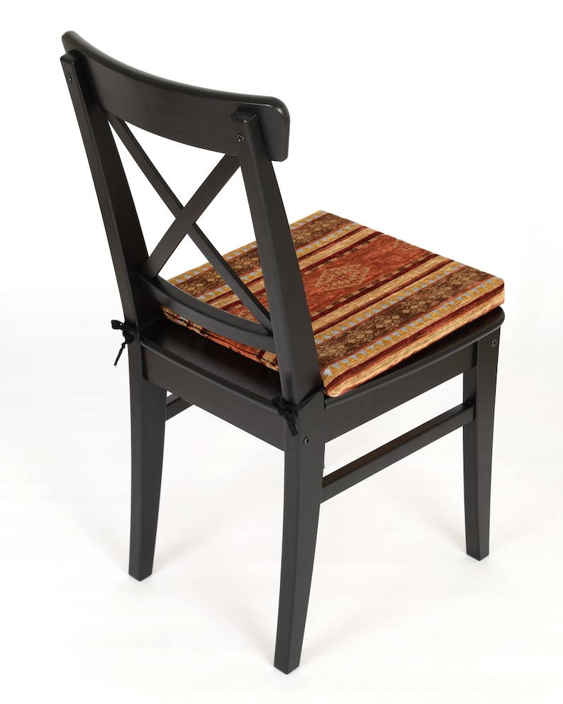Puede incluir: Silla de madera negra con un coj&iacute;n estampado en tonos rojos, naranjas y marrones. La silla tiene un dise&ntilde;o sencillo con un respaldo en forma de cruz.