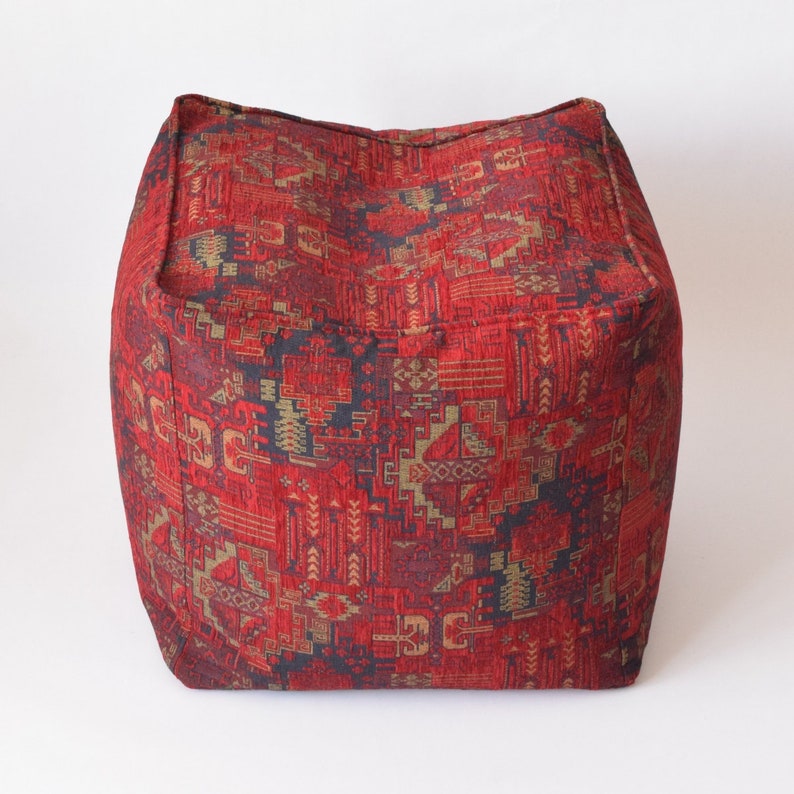 Pu&ograve; includere: Pouf quadrato rosso e oro con un design geometrico.