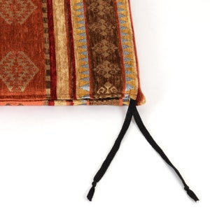 Puede incluir: Un primer plano de un coj&iacute;n de silla con estampado geom&eacute;trico en marr&oacute;n, naranja y dorado con cordones de amarre negros.