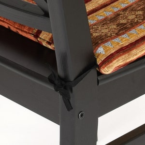 Puede incluir: Primer plano de una silla de madera negra con un coj&iacute;n estampado. El coj&iacute;n est&aacute; atado a la silla con correas negras.