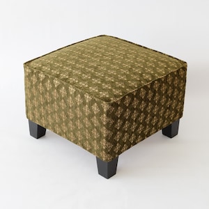 May include: A square ottoman with a green fabric upholstery featuring a repeating geometric pattern. The ottoman has four black wooden legs.