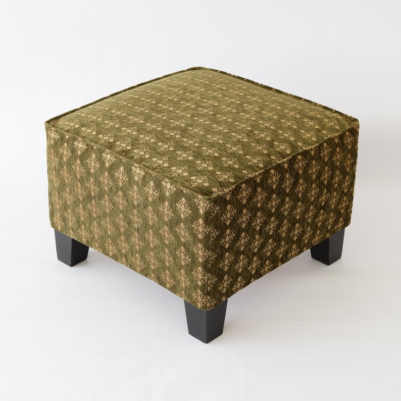 May include: A square ottoman with a green fabric upholstery featuring a repeating geometric pattern. The ottoman has four black wooden legs.