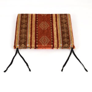 Puede incluir: Un coj&iacute;n de silla con estampado marr&oacute;n, naranja y beige con lazos negros. El coj&iacute;n tiene un dise&ntilde;o geom&eacute;trico de estilo suroeste.