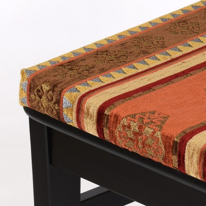 Puede incluir: Un otomano de madera negro con una parte superior de tela estampada de colores. La tela presenta un dise&ntilde;o geom&eacute;trico con rayas y un patr&oacute;n repetitivo.