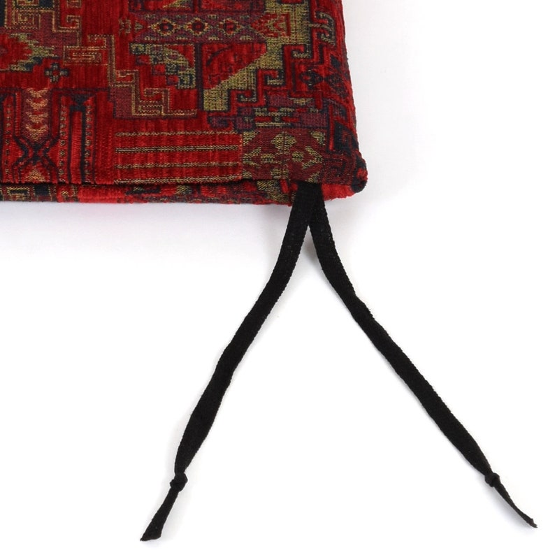 Peut inclure: Coussin rouge et or &agrave; motifs avec des cordons de serrage noirs. Le coussin a un design traditionnel.