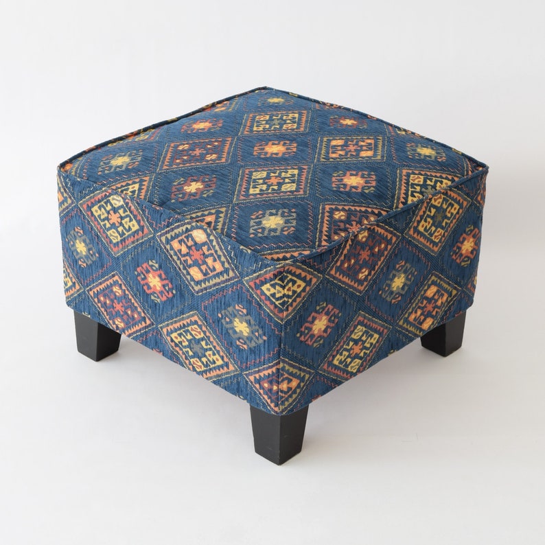 May include: A square ottoman with a blue fabric cover featuring a geometric pattern in shades of orange, yellow, and brown. The ottoman has four dark wood legs.