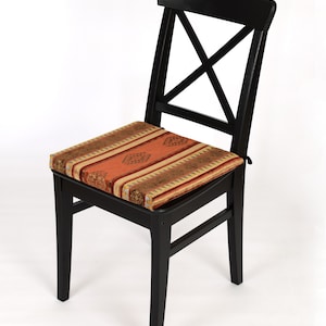 Puede incluir: Silla de madera negra con un coj&iacute;n estampado. El coj&iacute;n tiene un dise&ntilde;o geom&eacute;trico rojo, naranja y dorado.