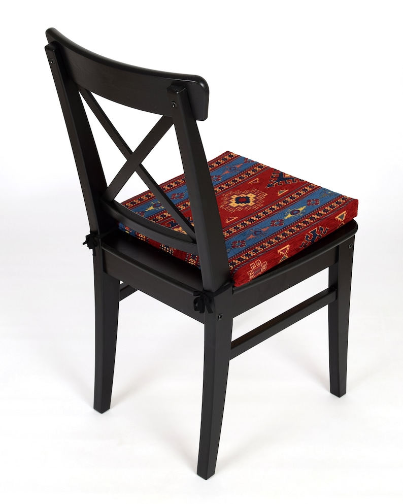 May include: Black wooden chair with a red, blue, and yellow patterned cushion. The chair has a cross-shaped back and a simple design.
