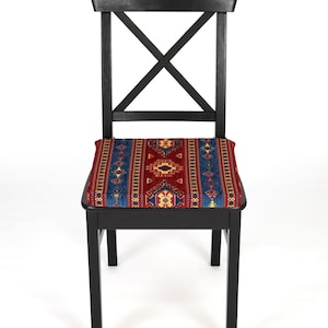 May include: A black wooden chair with a red, blue, and yellow patterned cushion. The chair has a simple, classic design with a cross-shaped back.