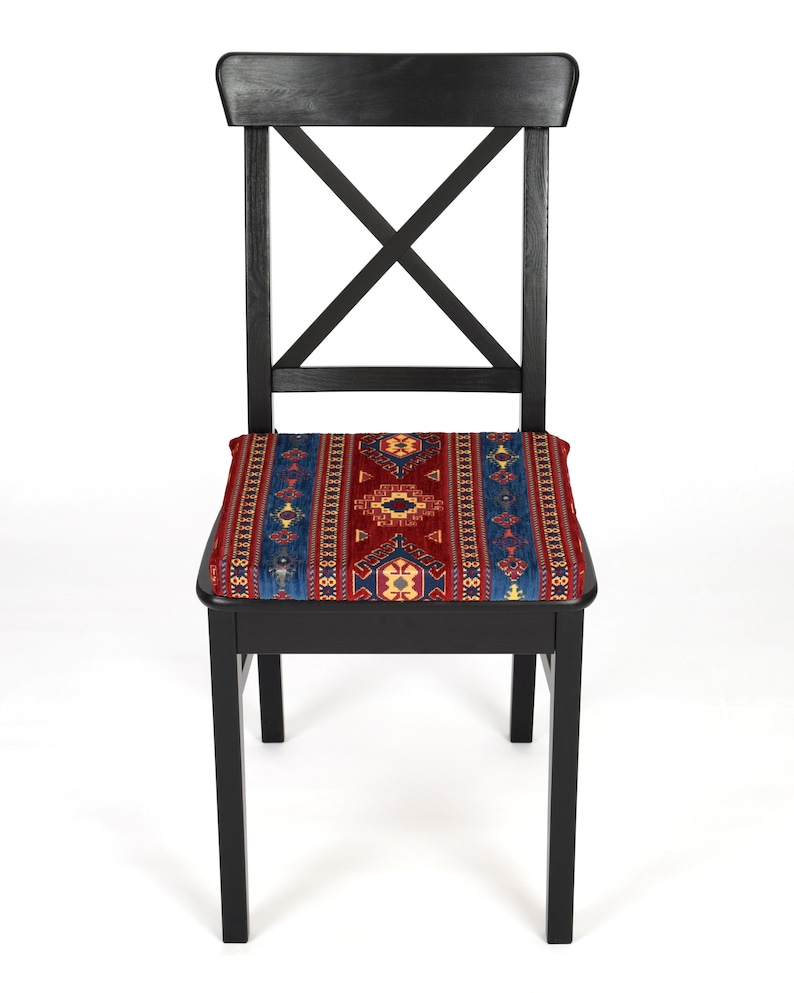 May include: A black wooden chair with a red, blue, and yellow patterned cushion. The chair has a simple, classic design with a cross-shaped back.