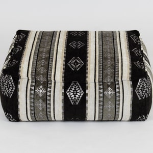 May include: Black and white striped ottoman with a geometric pattern. The ottoman is made of fabric and has a square shape.