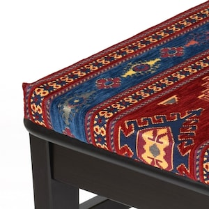 May include: A dark wood ottoman with a red, blue, and yellow patterned fabric top. The fabric has a traditional design with geometric shapes.