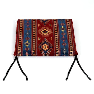 May include: A red, blue, and yellow patterned cushion with black ties. The cushion has a traditional geometric design.