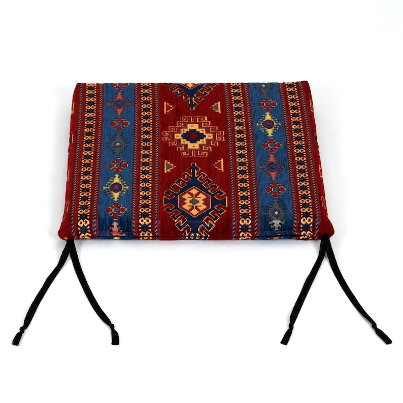 May include: A red, blue, and yellow patterned cushion with black ties. The cushion has a traditional geometric design.