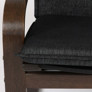May include: A dark brown wooden chair with a black fabric cushion. The cushion has a subtle textured pattern and a stitched edge.