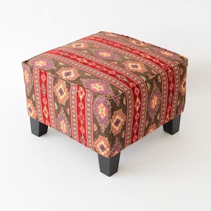 May include: A square ottoman with a brown, red and purple patterned fabric cover. The ottoman has four wooden legs.