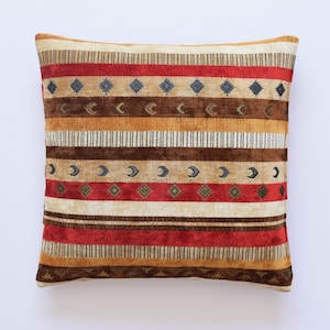 Puede incluir: Una almohada decorativa con un diseño de inspiración suroeste. La almohada presenta un patrón de rayas multicolores con formas geométricas y lunas crecientes.