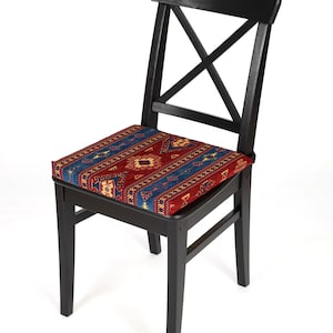 May include: A black wooden chair with a red, blue, and yellow patterned cushion. The chair has a simple, classic design with a cross-shaped back.