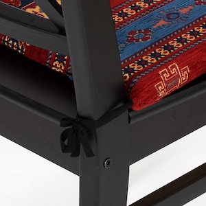 May include: Black wooden chair with a red, blue, and yellow patterned cushion. The cushion is secured with a black ribbon tied in a bow.