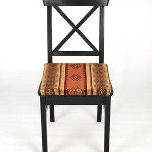 Puede incluir: Silla de madera negra con un coj&iacute;n de asiento tejido con un patr&oacute;n en tonos naranja, marr&oacute;n y beige.