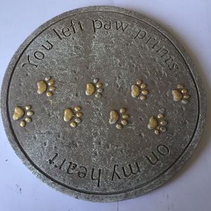 May include: A grey stone memorial with the text "You left paw prints on my heart" and gold paw prints.