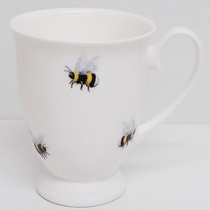 May include: White ceramic mug with a black handle and a design of yellow and black bumblebees.