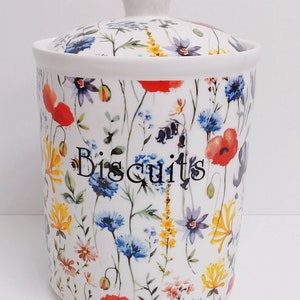 May include: White ceramic biscuit jar with a floral pattern featuring red poppies, blue cornflowers, and yellow wildflowers. The jar has a lid and says "Biscuits" in black lettering.