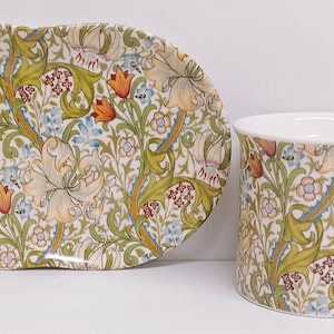 Könnte beinhalten: Ein weißes Porzellan-Teetassen- und Untertassen-Set mit einem Blumenmuster. Das Muster zeigt weiße Lilien, grüne Blätter und rote und blaue Akzente.