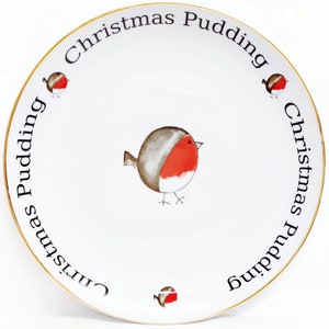 Może przedstawiać: Biały ceramiczny talerz ze złotą obwódką i wzorem świątecznego puddingu. Talerz przedstawia trzy rudziki i napis "Christmas Pudding" powtarzający się wokół krawędzi.