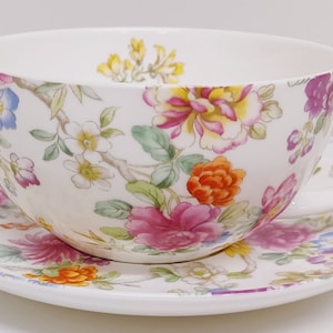 May include: A white teacup and saucer set with a floral pattern in shades of pink, yellow, orange, and blue.