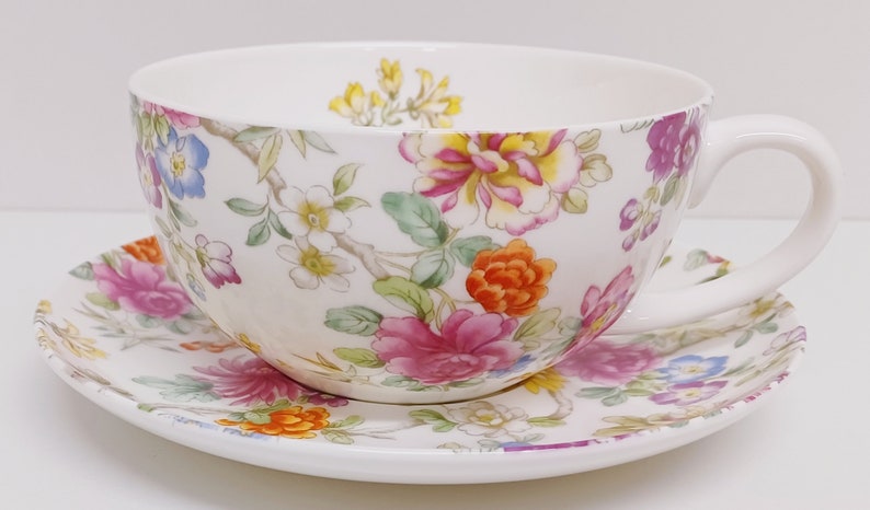May include: A white teacup and saucer set with a floral pattern in shades of pink, yellow, orange, and blue.