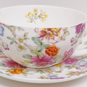May include: A white teacup and saucer set with a floral pattern in shades of pink, orange, yellow, and blue. The floral design features a variety of flowers and leaves.
