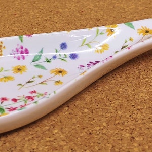 May include: White ceramic spoon rest with a floral pattern featuring pink, yellow, and purple flowers on a white background.