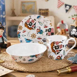May include: A white ceramic dinnerware set consisting of a plate, a bowl, and a mug, all decorated with a colourful pirate-themed pattern featuring ships, skulls, anchors, and treasure maps on a white background with a glossy finish.