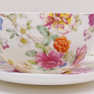May include: A white teacup and saucer set with a floral pattern in shades of pink, orange, yellow, and blue.