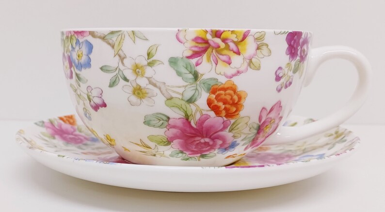 May include: A white teacup and saucer set with a floral pattern in shades of pink, orange, yellow, and blue.