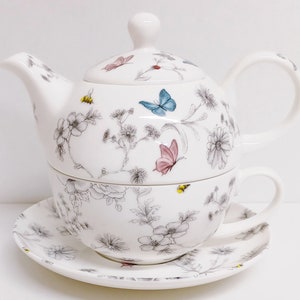 Peut inclure: Un ensemble théière et tasse en porcelaine blanche avec un motif floral et papillon. La théière a un couvercle et une poignée. La tasse a une poignée et repose sur une soucoupe assortie.