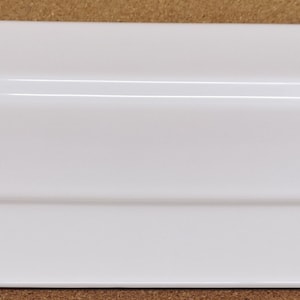 Könnte beinhalten: Eine weiße rechteckige Servierplatte mit einem erhöhten Rand und einer leicht gekrümmten Kante.