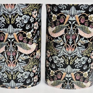 Può includere: Due tazze alte in ceramica con manici bianchi. Le tazze presentano uno sfondo nero con un motivo ripetuto di uccelli, fiori e bacche nei toni del rosa, verde e crema. Le tazze sono identiche.
