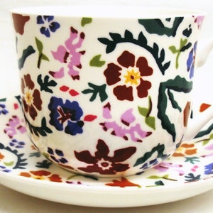 Op de afbeelding: Een wit theekopje en schotelset met een bloemenpatroon in tinten rood, paars, blauw, groen en oranje.