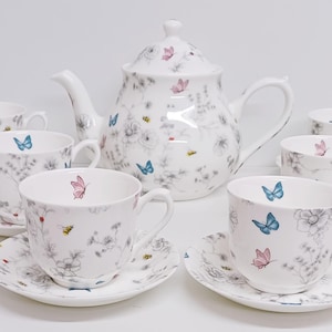 May include: A white porcelain tea set featuring a butterfly and floral design. The set includes a teapot, six cups, and six saucers.